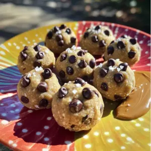 To make these high-protein chocolate chip cookie dough bites, you need the following ingredients: - 1 cup almond flour - 1/2 cup rolled oats - 1/2 cup protein powder (vanilla flavor) - 1/4 cup almond butter - 1/4 cup maple syrup - 1/4 cup mini dark chocolate chips - 1 teaspoon vanilla extract - Pinch of sea salt - 1-2 tablespoons almond milk (if needed) These ingredients are simple yet powerful. Almond flour gives a nice texture and is gluten-free. Rolled oats add heartiness and fiber. The protein powder boosts the nutrition in these bites. Almond butter brings healthy fats and a creamy texture. Maple syrup sweetens the mix, while mini dark chocolate chips add a delightful chocolatey flavor. The vanilla extract enhances the overall taste. Lastly, a pinch of sea salt balances the sweetness perfectly. If your dough feels too dry, you can add a bit of almond milk to achieve the right consistency. Start by taking a large mixing bowl. Add 1 cup of almond flour, 1/2 cup of rolled oats, and 1/2 cup of protein powder. Use a whisk or spoon to mix them well. Make sure no lumps remain. This step helps create a smooth base for your dough. In another bowl, mix 1/4 cup of almond butter, 1/4 cup of maple syrup, 1 teaspoon of vanilla extract, and a pinch of sea salt. Stir until everything blends into a smooth mix. This mixture gives the bites their sweet flavor and creamy texture. Now, gradually add the wet mixture to the dry ingredients. Stir well until a thick dough forms. If your dough feels crumbly, add 1 tablespoon of almond milk at a time. Keep mixing until the dough is smooth and holds together well. Next, use a small cookie scoop or your hands to form small balls from the dough. Place these balls on a baking sheet lined with parchment paper. Make sure they are evenly spaced. This helps them not stick together when they chill. Finally, put the baking sheet in the refrigerator. Chill the bites for about 30 minutes. This step helps them firm up and makes them easier to eat. After chilling, they are ready to enjoy as a tasty snack or treat! To get the right dough texture, you need to assess it. If your dough is too crumbly, it needs some moisture. Add 1 tablespoon of almond milk at a time. Mix well after each addition. Keep adding until the dough holds together. If the dough feels too wet, add a bit more almond flour or oats. This will help balance it out. You can boost the flavor in many ways. Try adding a pinch of cinnamon for warmth. A dash of nutmeg can bring in a cozy feel. You could also mix in some shredded coconut for extra texture. For a fun twist, consider adding dried fruit or nuts. Each choice gives your bites a unique taste. How you serve your bites matters. Use a colorful plate for a bright look. You can place them in a small basket for a rustic touch. Drizzle a bit of almond butter on top for a tasty finish. A sprinkle of sea salt can add a nice contrast. These small details make your bites more appealing. {{image_2}} You can change up the flavor of your cookie dough bites. Try using chocolate or peanut butter protein powder instead of vanilla. This small swap can give your bites a whole new taste. You can also add a dash of cinnamon or nutmeg for warmth. If you want a fruity twist, consider mixing in some dried fruit or coconut flakes. If you do not have almond flour, you can use oat flour or coconut flour. Both will work well and add their own unique flavor. For almond butter, try sunflower seed butter or cashew butter. These swaps can help with allergies or personal taste. They keep the bites tasty and healthy. In the fall, add pumpkin spice to your dough for a festive twist. A teaspoon of pumpkin puree can also add moistness and flavor. During the holidays, mix in some crushed peppermint or gingerbread spice. These seasonal flavors can make your bites special for any occasion. To keep your High-Protein Chocolate Chip Cookie Dough Bites fresh, store them in an airtight container. You can place them in the refrigerator or freezer. In the fridge, they stay good for about a week. For longer storage, freeze them. Just make sure to separate each bite with parchment paper to avoid sticking. These bites taste best within a week when stored in the fridge. If you freeze them, they can last up to three months. After thawing, enjoy them within a week for the best taste. These bites are best enjoyed cold or at room temperature. If you prefer them warm, pop them in the microwave for about 10-15 seconds. This will soften them nicely without losing their shape. Enjoy them as a quick snack or dessert anytime! These bites pack a protein punch. Each bite contains protein from the protein powder and almond butter. The almond flour and rolled oats add fiber, which helps with digestion. Plus, the mini dark chocolate chips provide antioxidants. This snack is great for energy and muscle recovery. They are tasty yet healthy, making them a good choice for any time of day. Yes, you can! Almond butter is great, but feel free to swap it out. Peanut butter, cashew butter, or sunflower seed butter work well too. Each nut butter adds a unique flavor and texture. Just make sure the nut butter is creamy for the best results. This flexibility lets you customize these bites to your taste. You can find pre-made options online or in stores. Look for brands like Quest or RXBAR. They offer tasty high-protein snacks. Check health food stores or major retailers like Amazon. Reading reviews can help you choose a product you’ll enjoy. You’ve learned how to make tasty and healthy protein bites. We covered easy ingredients, step-by-step instructions, and fun tips. You can customize them with different flavors and options. Proper storage helps keep them fresh longer. Enjoy these bites as a snack or treat. Remember to experiment with your favorite nuts or spices. With a little creativity, you can create your perfect protein snack. Now, grab your ingredients and start making delicious bites today!